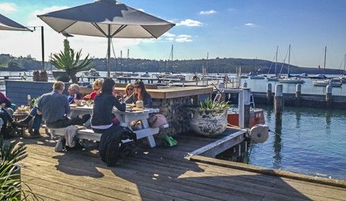 People sitting outside at a table at a cafe on the Northern Beaches of Sydney and overlooking boats on the water.